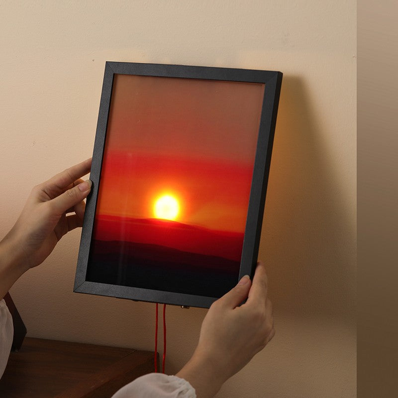 Person holding a framed artwork of a sunset.