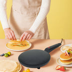 Person making pancakes with a black crepe maker on a yellow background