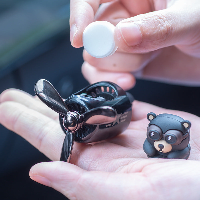Black propeller model airplane and bear-shaped toy held in a hand with a blurred background